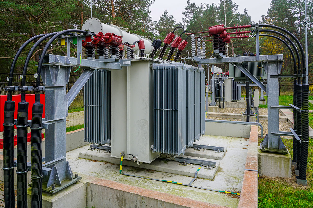 Two oil-immersed power transformers with red bushings and heavy black cabling inside a fenced electrical substation