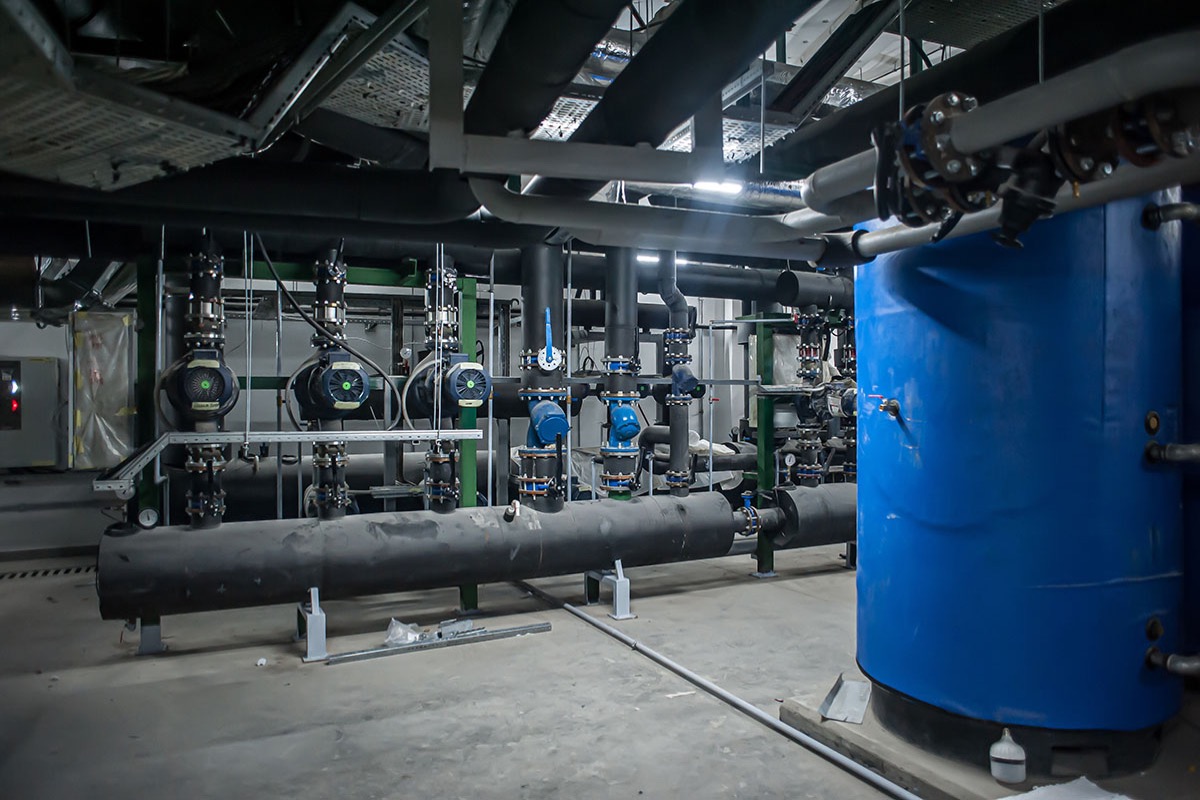 An industrial plant room with circulation pumps, insulated pipework and a large blue storage tank