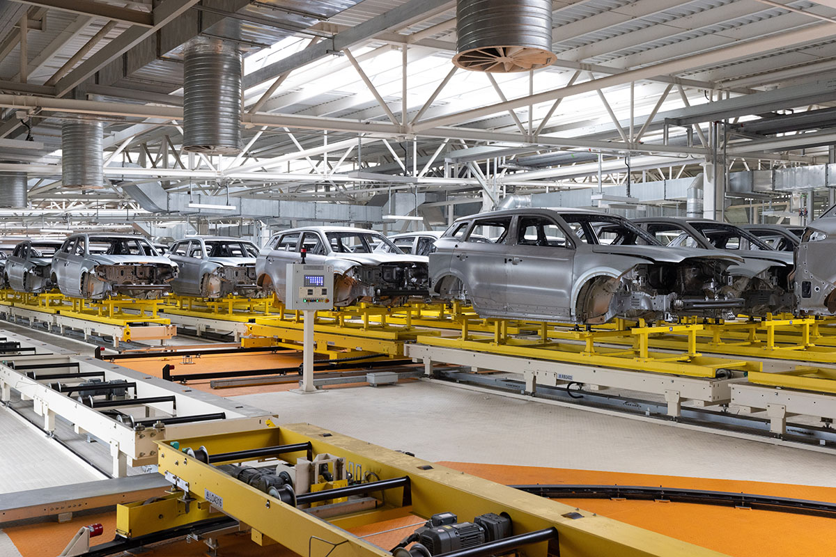 Unpainted car bodies on carriers along an automated assembly line in a bright factory hall with no workers in view