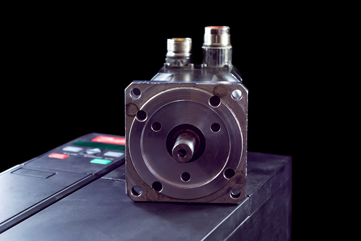 An industrial AC servo motor with its mounting flange and output shaft facing the camera, resting on a motor drive unit against a black background