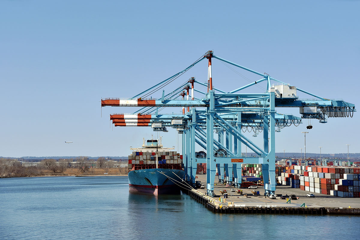 Blue gantry cranes working a berthed container ship beside stacked containers at a U.S. port terminal